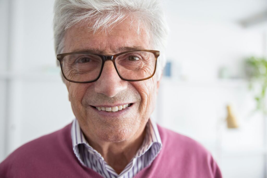 Close-up headshot of a smiling senior man wearing eyeglasses, indoors in Portugal.
